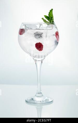 Verricello di cristallo pieno di ghiaccio e bevanda con lampone maturo guarnito con menta su sfondo bianco Foto Stock