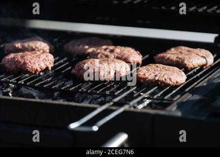 Poche frittatine di hamburger crudo arrostendo sulla griglia di barbecue all'esterno sotto la luce del sole Foto Stock