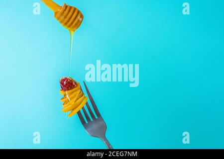 minuscoli pancake su una forchetta con fragole fresche, banana, cioccolato, patatine di cocco e miele in un piatto su sfondo blu. tendenza alimentare 2020. Foto Stock