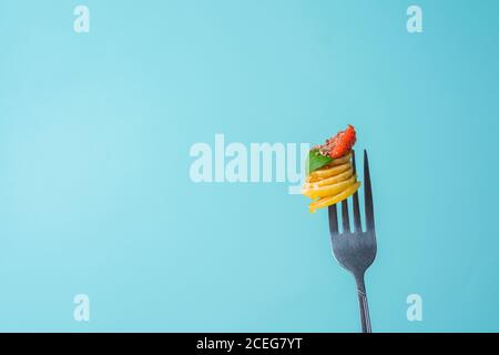 minuscoli pancake su una forchetta con fragole fresche, banana, cioccolato, patatine di cocco e miele in un piatto su sfondo blu. tendenza alimentare 2020. Foto Stock