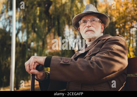 Foto di sognante riposo vecchio uomo rilassante sera autunno forest park siede panchina con bastone a piedi guardare sogno passato capi outerwear stagionali Foto Stock