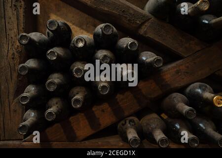 Delicata ed elegante volta di vino piena di bottiglie sdraiate al buio ripiani in legno con luce che splende dall'alto Foto Stock