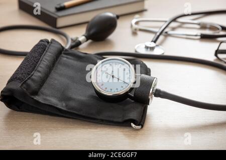 Apparecchiatura per la misurazione della pressione sanguigna, controllo dell'ipertensione. Stetoscopio medico e sfigmomanometro sulla scrivania dell'ufficio medico, vista dell'armadio. Foto Stock