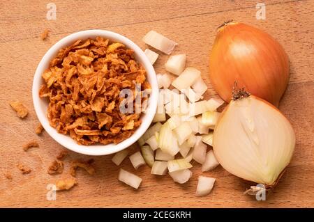 Cipolle fritte croccanti in una ciotola bianca in ceramica, un mucchio di cipolle tagliate di fresco e cipolla dimezzata su tavola di legno. Vista dall'alto. Foto Stock