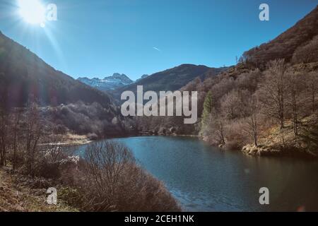 Vista pittoresca del lago vicino a foresta secca, belle montagne e cielo blu in giornata di sole a Canfranc-Station, Huesca, Spagna Foto Stock