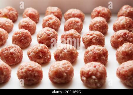 Le polpette crude appena cotte si trovano su una tavola da cucina di plastica bianca. Foto Stock