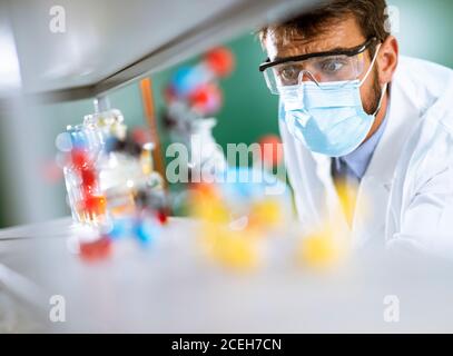 Giovane ricercatore con occhiali di protezione che controlla le provette nel laboratorio Foto Stock