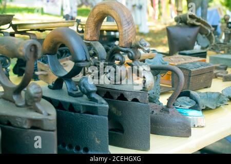 Ferri da stiro in metallo antico e altri articoli d'epoca sul mercato delle pulci o festival. Oggetti da collezione memorabilia concetto. Ferro con manico vintage Foto Stock