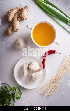 Ingredienti piccanti per zuppe asiatiche. Zenzero, aglio, brodo di pollo e carne, peperoncino rosso, coriandolo e scalione, tagliatelle giapponesi. tessuto bianco st Foto Stock
