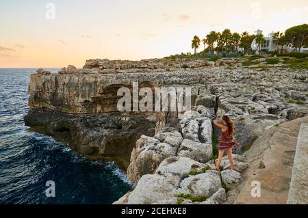 Donna che guarda le scogliere di SA Torre cape al tramonto con una villa di lusso sullo sfondo (Santanyí, Maiorca, Isole Baleari, Mar Mediterraneo, Spagna) Foto Stock