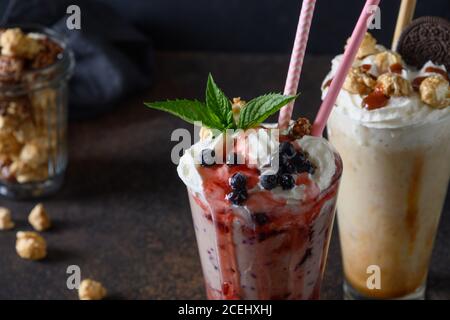 Delizioso frullato di bacche guarnito con panna montata, mirtilli, marmellata gocciolante al buio. Primo piano. Foto Stock