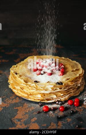 Frittelle russe con bacche cosparse di polvere di zucchero davanti a fondo scuro. Settimana dei pancake - l'antico festival slavo di vedere fuori il wi Foto Stock