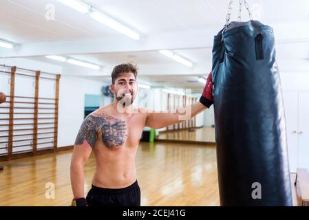 Ritratto di un giovane pugile appoggiato sul sacchetto del punzone in palestra Foto Stock