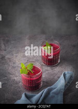 Due bicchieri di frullato di barbabietola con foglie di menta su un tavolo scuro. Scatto con spazio per la copia. Foto Stock