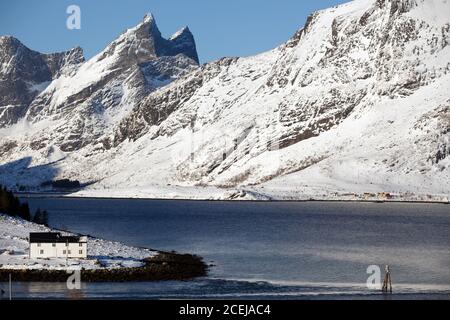 tradizionale casa norvegese in legno per stare sulla riva del fiordo e le montagne in lontananza. Isole Lofoten. Norvegia. Foto Stock