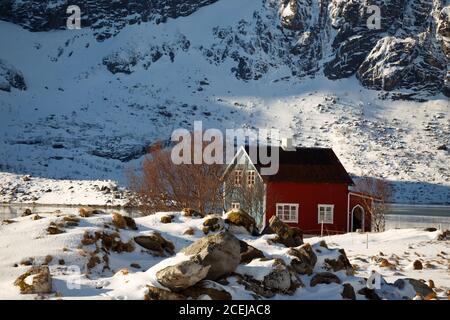 tradizionale casa norvegese in legno per stare sulla riva del fiordo e le montagne in lontananza. Isole Lofoten. Norvegia. Foto Stock