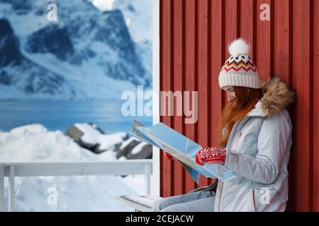 Ragazza turistica si siede vicino rorbu con una mappa a isole Lofoten. Norvegia Foto Stock