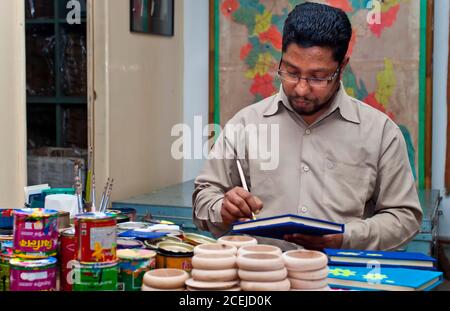 Bangladesh – 16 febbraio 2014: Un artista artigianale sta dipingendo su una copertina di libri fatti a mano in-home studio Workspace a Dhanmondi, Dhaka. Foto Stock