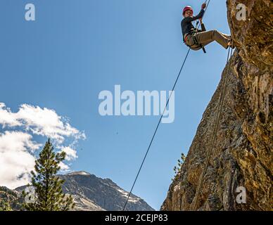 Giovane uomo che ruggito su una roccia di fronte a Piz Palü. La discesa di fronte al massiccio del Piz Palü è la ricompensa alla fine del corso introduttivo di arrampicata. Arrampicata su roccia a Pontresina, Svizzera Foto Stock