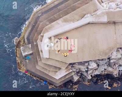 Da sopra colpo di gente anonima che forma il cerchio mentre in piedi su un edificio in cemento su una splendida scogliera rocciosa vicino al mare ondeggiante Foto Stock