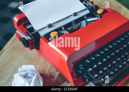 Macchina da scrivere in primo piano di colore rosso brillante con foglio di carta vuoto inserito e. carta sgualcita Foto Stock
