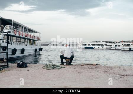 Vista posteriore di un adulto seduto sul molo vicino all'acqua e navi e la pesca a Istanbul, Turchia Foto Stock