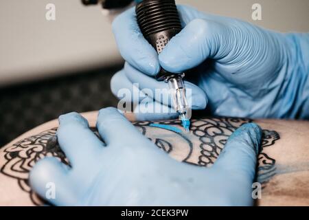 Primo piano delle mani in guanti in lattice utilizzando la macchina a. tatuaggio a colori con inchiostro blu in studio Foto Stock
