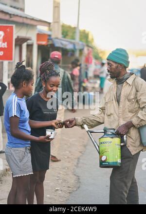 Ranohira, Madagascar - 29 aprile 2019: Uomo malgascio sconosciuto che vende bevande a base di frutta a due giovani ragazze sulla strada, versandola direttamente dalla lattina spolverata Foto Stock