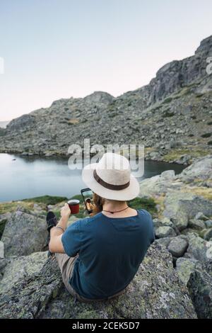 Giovane uomo seduto su rocce vicino al lago Foto Stock