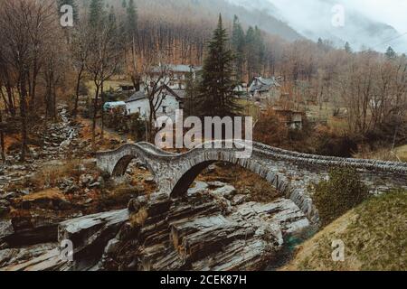 Piccolo ponte ondulato in pietra nel villaggio in autunno. Foto Stock