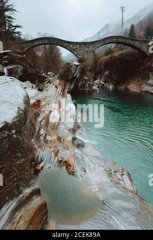 Vista sul piccolo ponte ondulato in pietra sul fiume blu nella natura. Foto Stock