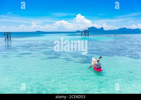 Vista posteriore maschile barca su canoa con pagaia su Amazing Mare azzurro e cielo blu in Malesia Foto Stock