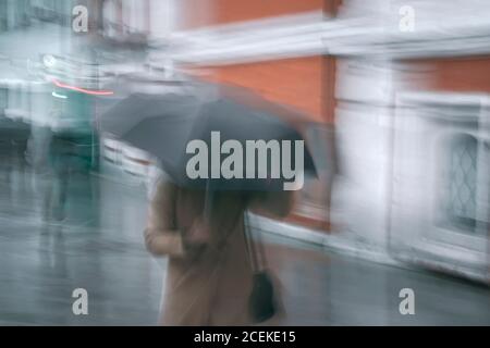 Astratto sfondo offuscato di donna che si fa male sotto ombrello, serata piovosa, stile di vita nella città moderna Foto Stock