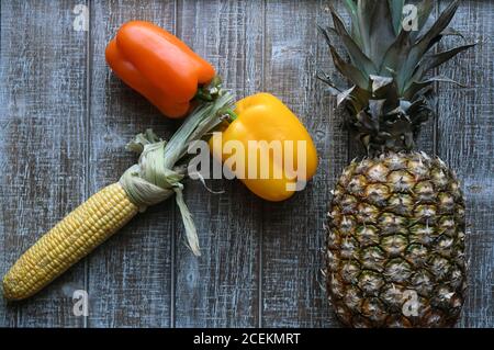 PARTY MIX: Un mix di frutta e verdura che includono peperoni, ananas e mais sulla pannocchia sono disposti insieme su un tagliere di legno. Foto Stock