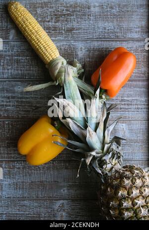 PARTY MIX: Un mix di frutta e verdura che includono peperoni, ananas e mais sulla pannocchia sono disposti insieme su un tagliere di legno. Foto Stock