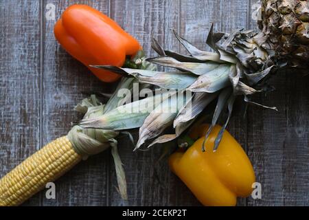 PARTY MIX: Un mix di frutta e verdura che includono peperoni, ananas e mais sulla pannocchia sono disposti insieme su un tagliere di legno. Foto Stock