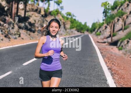 Eseguire l'esercitazione fit Asian donna jogging correre su strada di montagna fuori in natura. Felice ragazza che si esercita indossando viola moda top sportswear Foto Stock