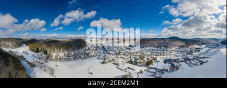 Città idilliaca in un inverno innevato, girato dall'alto, un drone sparato nell'Alb Svevo con colline e una parte di una foresta. Foto Stock