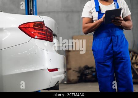 Un addetto all'officina con una clipboard cerca danni su una macchina Foto Stock