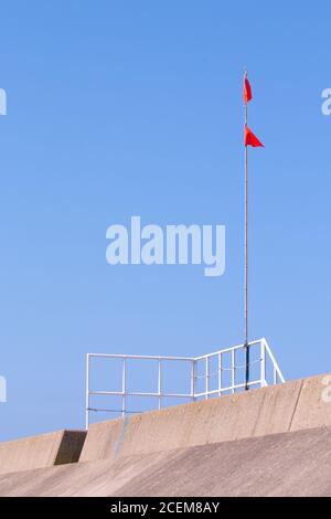 Le bandiere rosse indicano l'accesso alla spiaggia in cima a una costa barriera di protezione Foto Stock