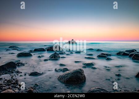 Lunga esposizione stagionale con onde schiumose che spruzzano contro una roccia shore Foto Stock