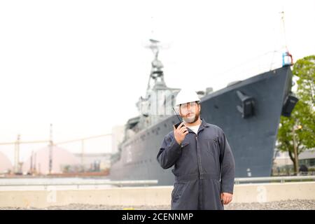 Ufficiale del ponte marino che parla da radio walkie talkie e in piedi vicino nave offshore in pankground. Foto Stock