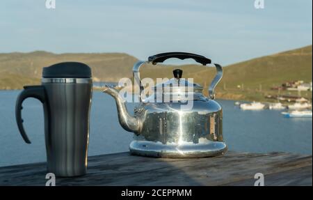 teiera in metallo antico e tazza da viaggio sullo sfondo del lago. fuoco selettivo. concetto di ricreazione all'aperto. Foto Stock