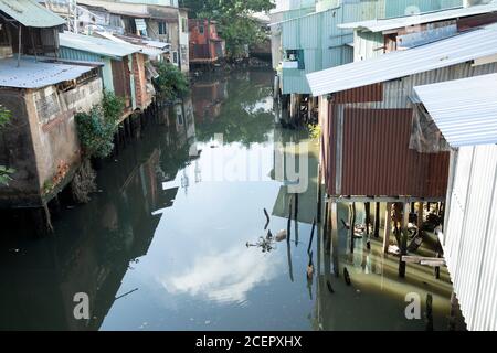 Case in mattoni, legno e ferro ondulato e su palafitte lungo un canale stretto nella città di ho Chi Minh, Vietnam Foto Stock