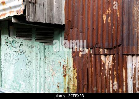 tessuti di ferro corrugato, legno, peeling vernice su una vecchia casa in un quartiere povero Foto Stock