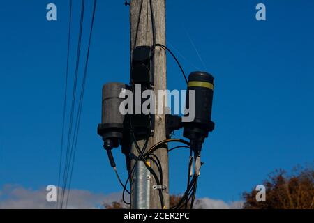 Un paio di giunti per cavi in fibra ottica impermeabili montati su un palo accanto a una strada trafficata in una posizione rurale. Foto Stock