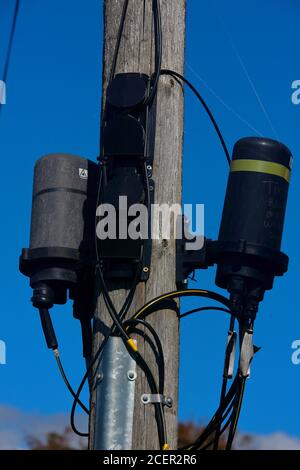 Un paio di giunti per cavi in fibra ottica impermeabili montati su un palo accanto a una strada trafficata in una posizione rurale. Foto Stock