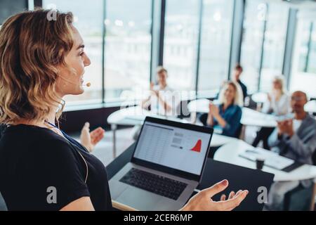 Donna d'affari che parla con gli uomini d'affari da un podio. Dirigente femminile che si rivolge a gruppi di professionisti in una conferenza. Foto Stock