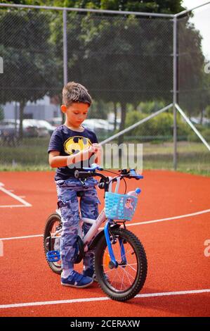 POZNAN, POLONIA - 30 agosto 2020: Ragazzo con una camicia Batman seduta su una bicicletta su un campo sportivo Foto Stock