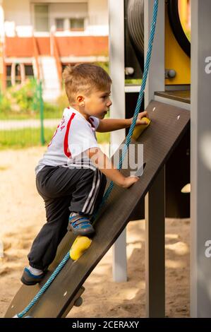 POZNAN, POLONIA - 30 agosto 2020: Ragazzo caucasico polacco di tre anni che arrampica su un equipaggiamento con corda in un parco giochi. Foto Stock